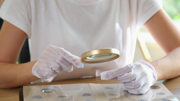 Femme numismate en gants examine sa collection de pièces à table libre de femme à la recherche