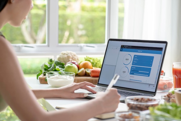 Femme nutritionniste professionnelle travaillant et vérifiant les données d'un ordinateur portable avec une variété de fruits noix légumes et compléments alimentaires sur la table