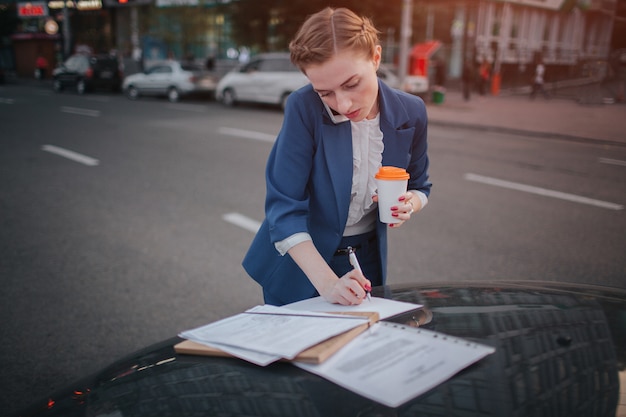 La femme occupée est pressée, elle n'a pas le temps, elle va parler au téléphone en déplacement. Femme d'affaires faisant plusieurs tâches sur le capot de la voiture. Homme d'affaires multitâche.