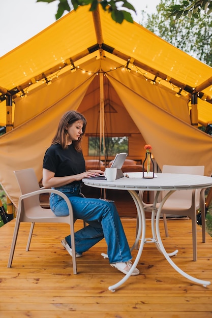 Femme occupée indépendante utilisant un ordinateur portable sur une tente de glamping confortable par une journée ensoleillée Tente de camping de luxe pour les vacances d'été en plein air et les vacances Concept de style de vie