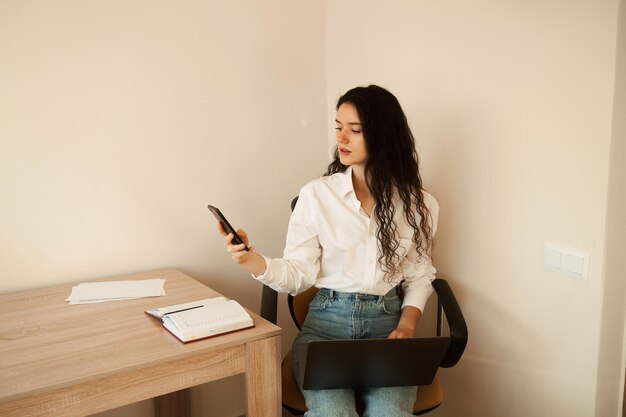 Femme occupée parlant par téléphone et travaillant sur un ordinateur portable sur les genoux à la maison Travail à distance des heures supplémentaires Fille fatiguée patron travaillant en ligne avec des collègues à la maison