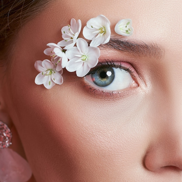 Femme d'oeil de maquillage de printemps avec des fleurs blanches. Maquillage pour les yeux de beauté florale créative. Fleurs d'été cosmétiques pour les cils