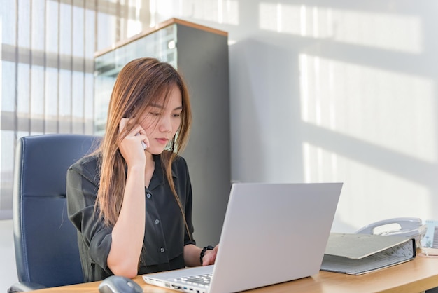 Une femme officier asiatique parle au téléphone et travaille avec un ordinateur portable sur le bureau du bureau