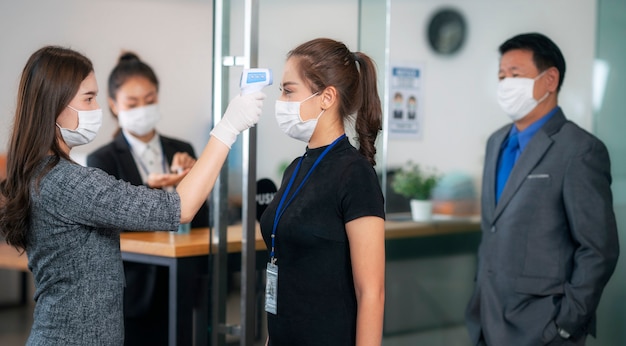 Femme officier utiliser un thermomètre scanner vérifier la température de toute personne avant de passer au bureau à l'intérieur pour travailler