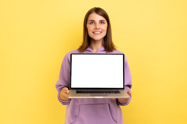 Femme optimiste positive debout montrant un ordinateur portable avec un écran blanc vide pour la promotion