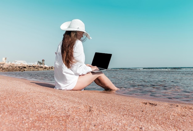 Une femme avec un ordinateur portable sur un sable se repose et travaille comme pigiste