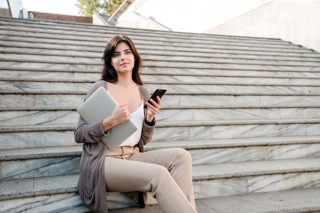 Femme avec ordinateur portable et téléphone dans la ville