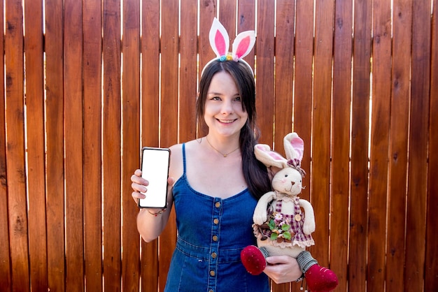 Femme avec une oreille de lapin de Pâques tenant un téléphone portable et un lapin de Pâques