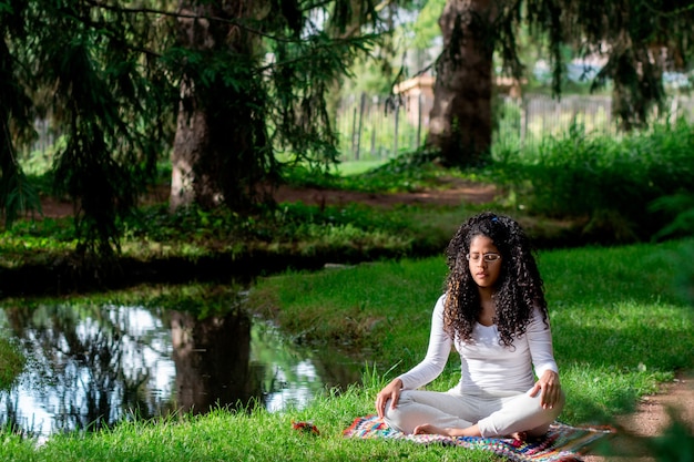 Femme d'origine africaine pratiquant le yoga à côté de l'eau dans le parc