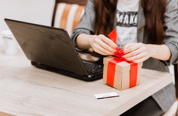 La femme ouvre le cadeau. Il y a un ordinateur portable et une carte de crédit sur la table. Achats en ligne et concept de cadeau. photo horizontale