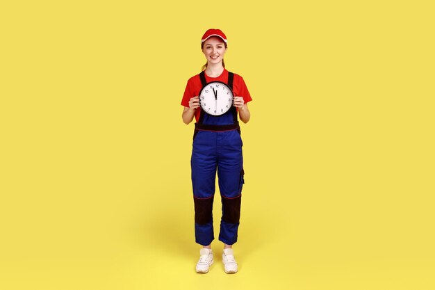 Femme ouvrière debout avec une grande horloge murale dans les mains regardant la caméra avec le sourire