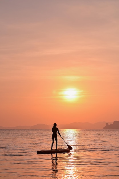 Une femme pagayant un supboard dans la mer au coucher du soleil