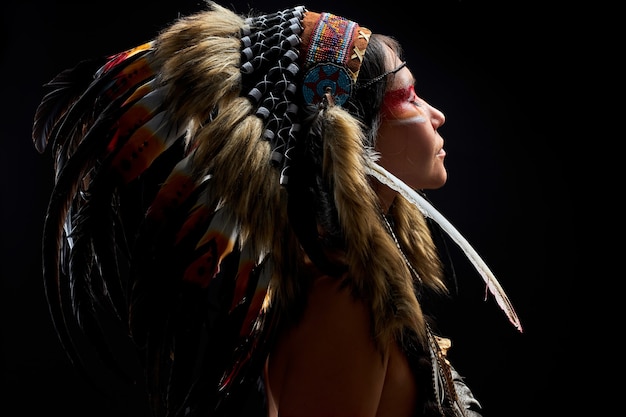 Photo femme païenne est un chaman sur le mur noir, vue latérale sur la femme avec des plumes sur les cheveux faisant le rituel