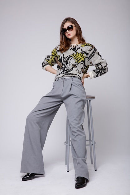 Femme en pantalon gris chemisier bottes accessoires bicolores sur fond blanc cheveux bruns Studio Shot