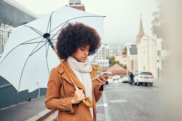 Femme parapluie et smartphone en ville pour la création de contenu sur les réseaux sociaux en automne Jeune influenceur réseautage numérique ou étudiant lire la communication Web en ligne sur téléphone mobile dans la ville urbaine