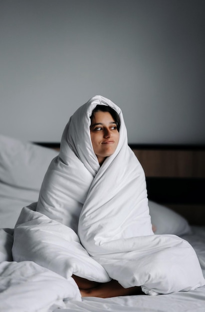 Photo femme paresseuse enveloppée dans une couverture douce assise dans un lit douillet