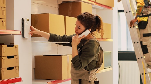 Femme parlant au répartiteur dans l'entrepôt, répondant à un appel téléphonique fixe pour discuter avec le siège de la distribution et de la production de marchandises.