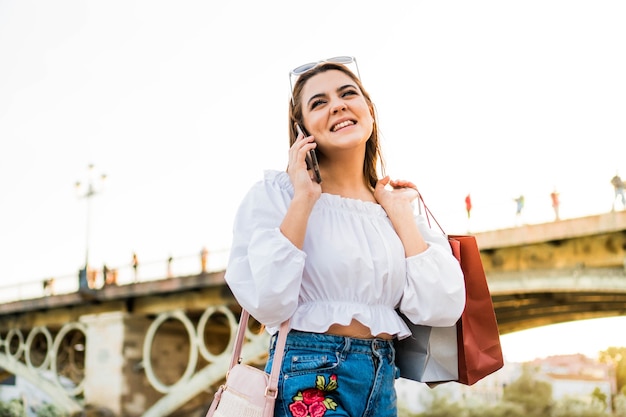 Femme parlant au téléphone dans un coucher de soleil après le shopping Jeune fille utilisant son portable