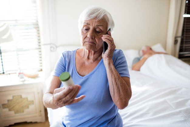 Femme parlant au téléphone mobile et tenant une bouteille de prescription de médicaments dans la chambre à coucher à la maison