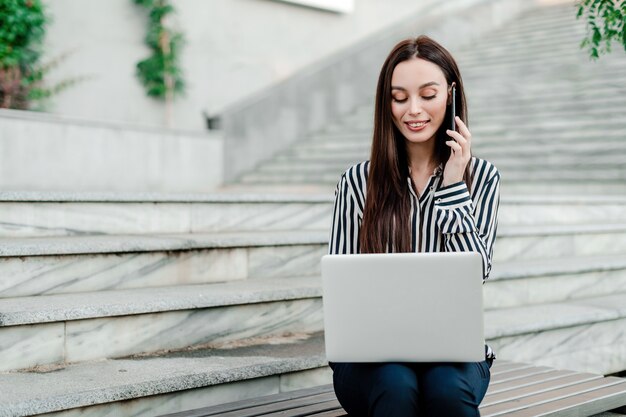 Femme parlant au téléphone et travaillant sur un ordinateur portable à l'extérieur