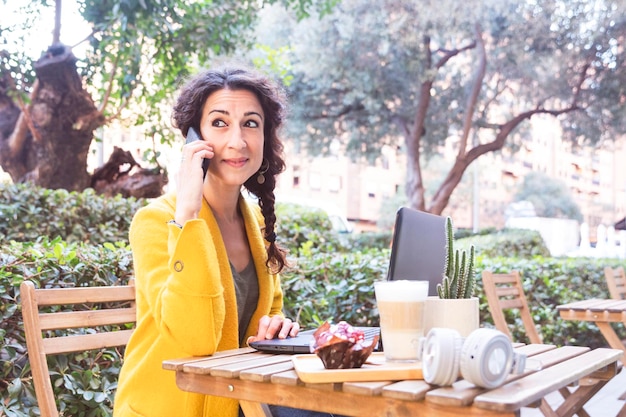 Femme parlant sur mobile assise sur une terrasse d'une cafétéria