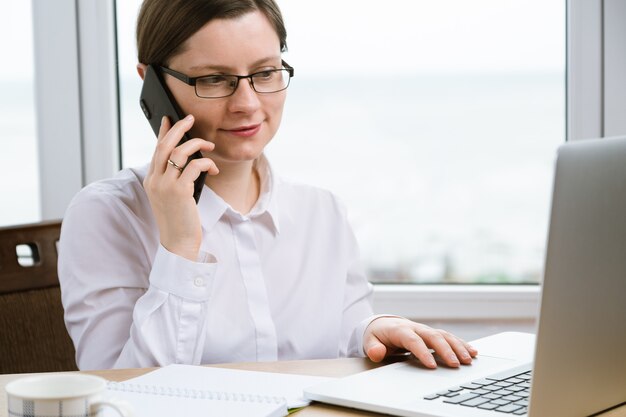 Femme parlant par téléphone et utilisant le pavé tactile sur un ordinateur portable. Travail à domicile en quarantaine.