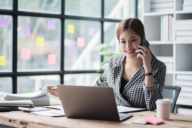 Photo une femme parle sur son téléphone portable alors qu'elle est assise à un bureau avec un ordinateur portable