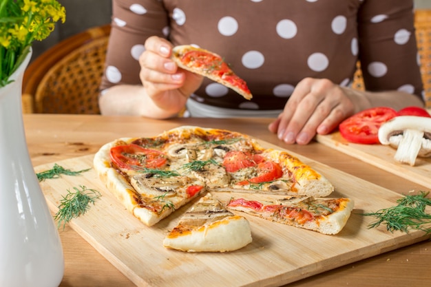 Femme avec une part de pizza rectangulaire faite maison Margherita aux champignons.