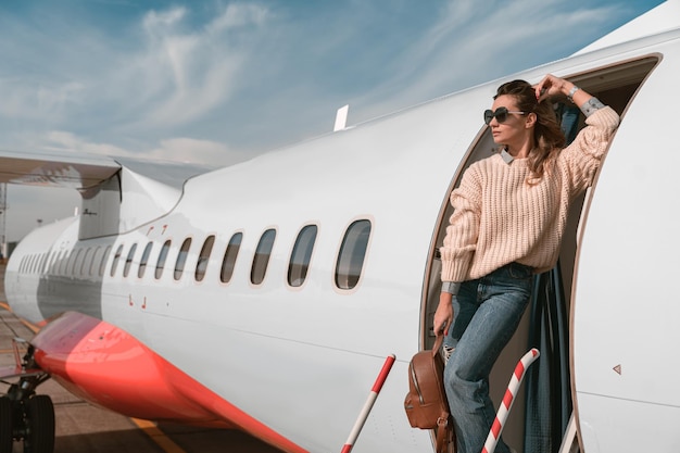 Femme passagère à lunettes de soleil debout sur les escaliers de l'avion à l'aéroport et regardant au loin