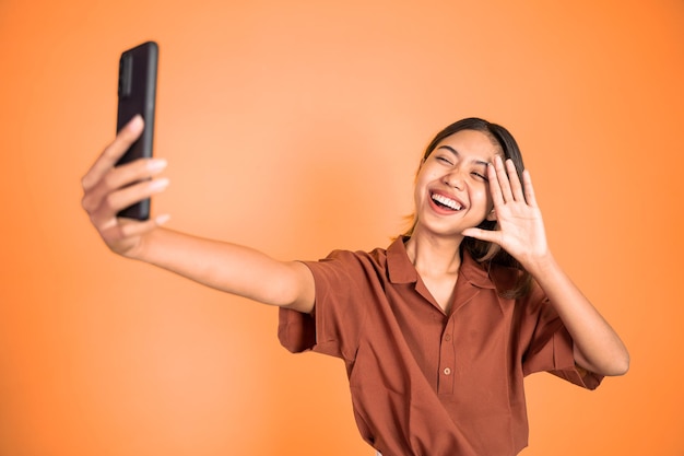 Une femme passe un appel vidéo à l'aide d'un téléphone portable en disant bonjour le geste