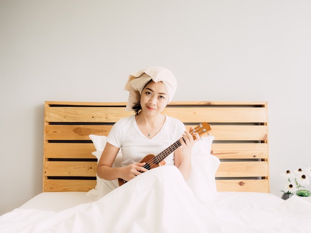 La femme passe une bonne journée de détente avec son ukulélé au lit.