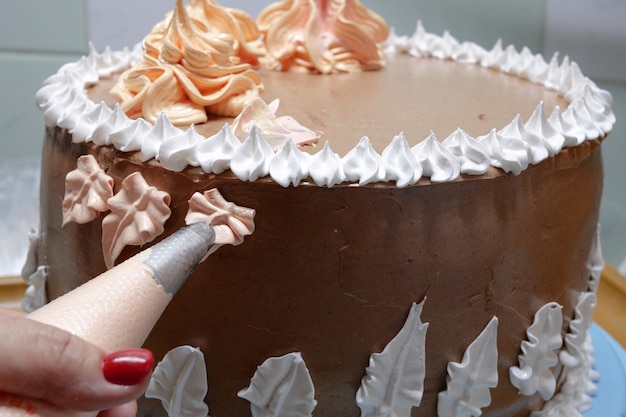 La femme pâtissière verse de la crème sur le gâteau à l'éponge en utilisant le sac de pâtisserie en gros plan Le pâtissier cuit un gâteau fait maison cuit et cuit à la maison