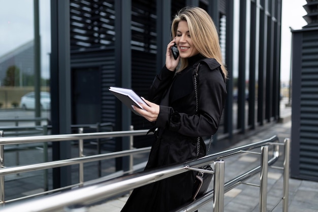 Femme patronne en vêtements de travail sur le fond de la façade en verre d'un immeuble de bureaux parle sur