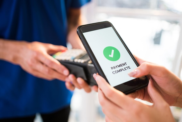 Femme payant une facture via un smartphone à l'aide de la technologie de paiement sans contact Client satisfait payant via un téléphone portable à l'aide de la technologie NFC