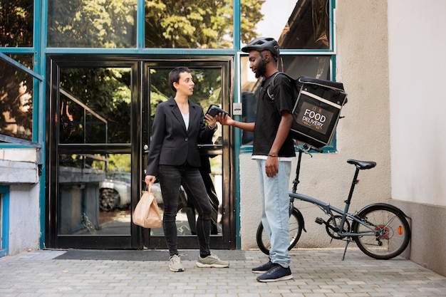 Femme payant pour le service de livraison de nourriture au bureau avec smartphone, terminal pos sans contact, paiement par portefeuille mobile. Courrier livrant un employé de repas à emporter au restaurant devant le bâtiment de l'entreprise