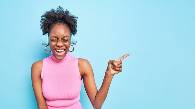 Une Femme à La Peau Foncée Ravie Avec Des Rires Aux Cheveux Bouclés Exprime Positivement Des émotions Heureuses Indique Un Espace Vide