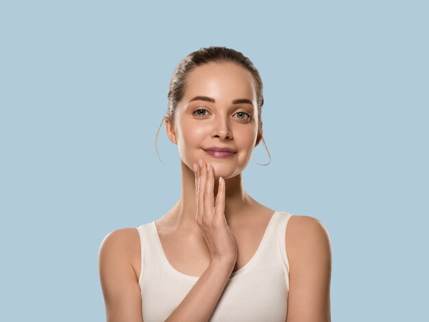 Femme de peau saine de beauté touchant son visage. Belle femelle. Fond de couleur. Bleu