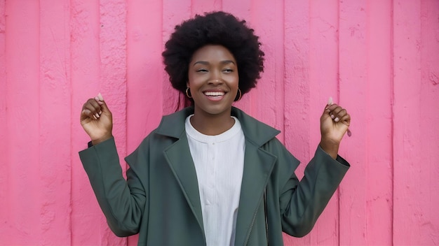 Une femme de peau sombre joyeuse célèbre la bonne nouvelle vêtue de vêtements de dessus sourit joyeusement pose en rose