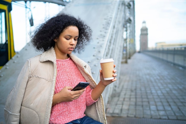 Femme à la peau sombre pensive tenant un smartphone mobile dans ses mains femme afro-américaine sérieuse dr...