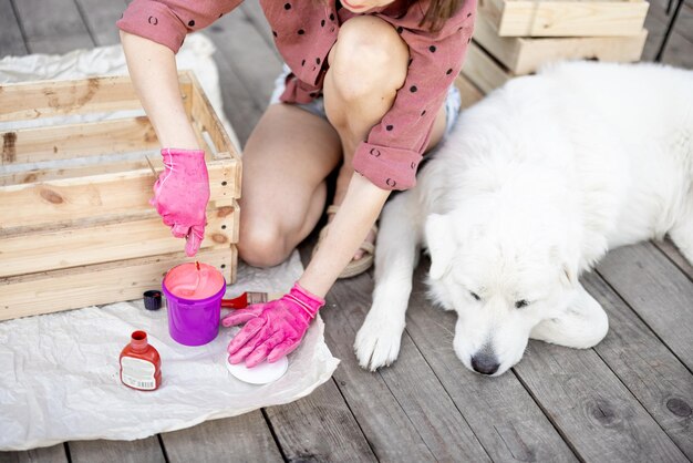 Femme peignant une boîte en bois assise avec un chien sur une terrasse