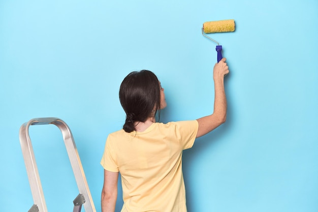 Femme peignant un mur bleu depuis une échelle