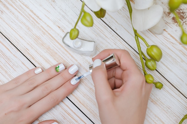 Femme peignant ses ongles en couleur blanche.