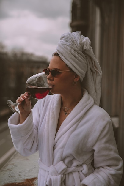 Une femme en peignoir blanc et lunettes de soleil boit du vin