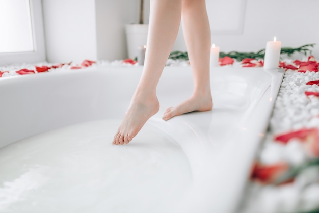 Femme en peignoir blanc plonge les jambes dans la baignoire