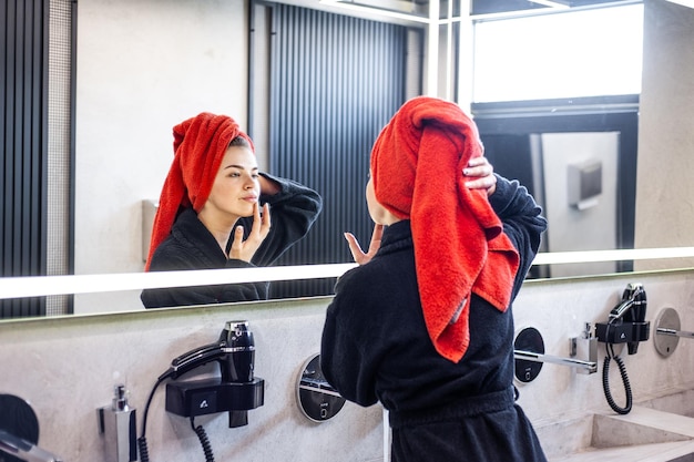 Une femme en peignoir se regarde dans un miroir et se brosse les cheveux.