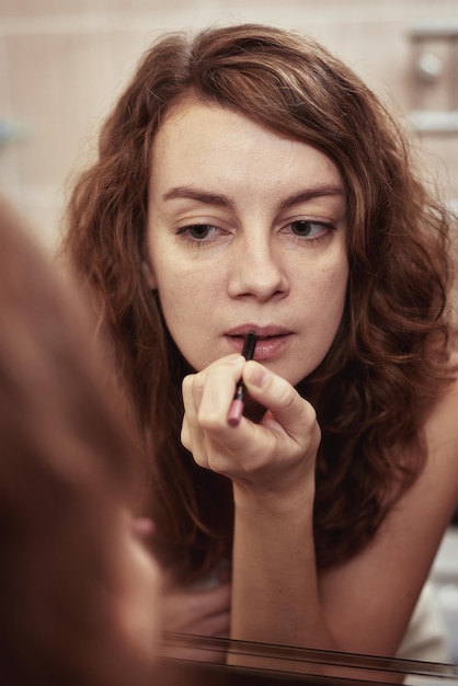 Femme peindre ses lèvres avec du rouge à lèvres devant le miroir