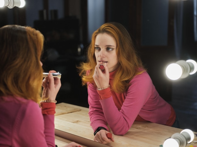 Femme peint ses lèvres avec du rouge à lèvres près du miroir