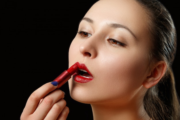 Une femme peint ses lèvres avec du rouge à lèvres rouge
