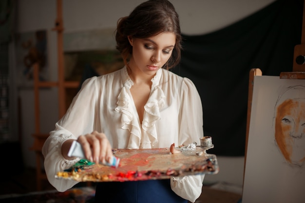 Femme peintre ajoute une couleur à la palette en studio.