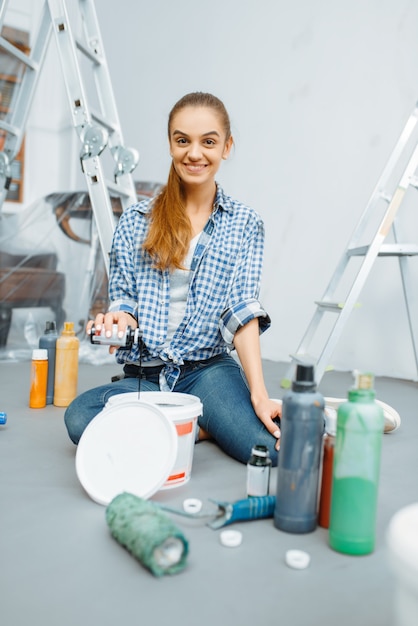 Une femme peintre en bâtiment mélange des peintures dans un seau. Réparation à domicile, femme qui rit en train de rénover un appartement, rénovation de décoration de chambre